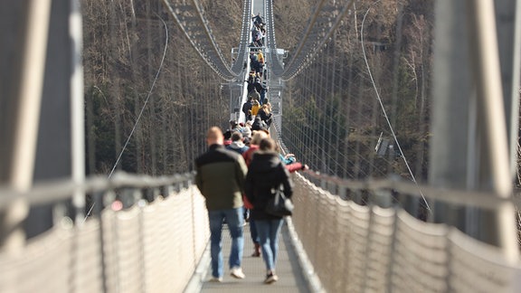 Besucher gehen bei strahlendem Sonnenschein an der Rappbodetalsperre bei Hasselfelde über eine Hängebrücke. 