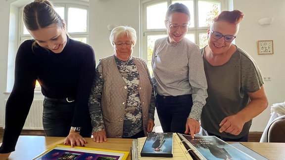 Vier Menschen betrachten auf einem Tisch liegende Bilder und Broschüren.