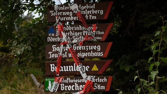 Ein Absperrband der Polizei verdeckt auf einem Wegweiser den Schriftzug "Brocken". Aufgrund eines Waldbrandes am Königsberg unterhalb vom Brocken im Harz ist die Zufahrt gesperrt.