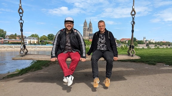 Lars Wohlfarth und André Plaul, auf einer Schaukel, vor dem Magdeburger Dom, sitzend