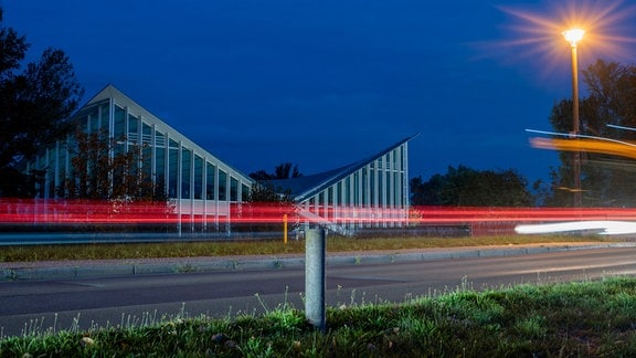 Vor der Hyparschale in Magdeburg sind Lichtstreifen von vorbeifahrenden Autos zu sehen.
