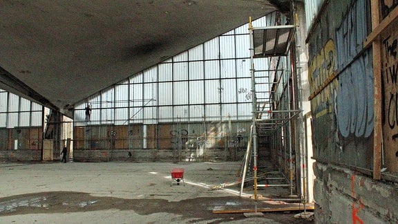 Leerstehende Halle mit Betonfußboden, Glasfront und Gerüst an einer Wand