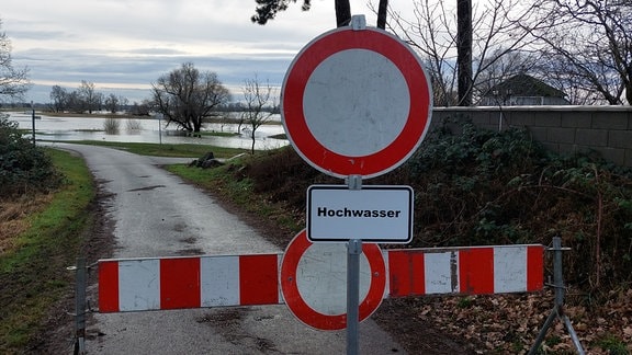 Eine Barriere und ein rundes, rot umrandetes Schild mit der Aufschrift Hochwasser versperren einen Radweg.