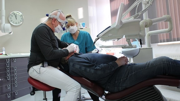 Zahnarzt und Fachangestellte behnadeln einen älteren Man im Behandlungsstuhl
