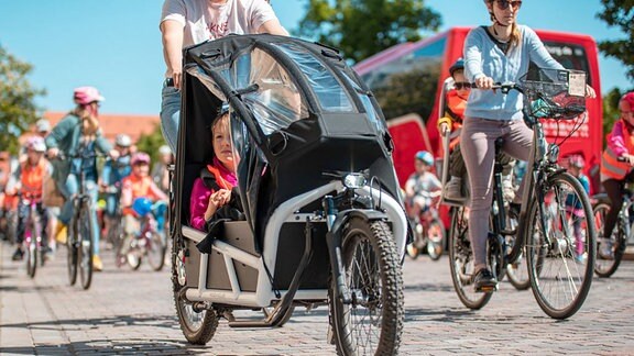 Lastenräder und Fahrräder mit Erwachsenen und Kindern auf Kopfsteinpflaster.