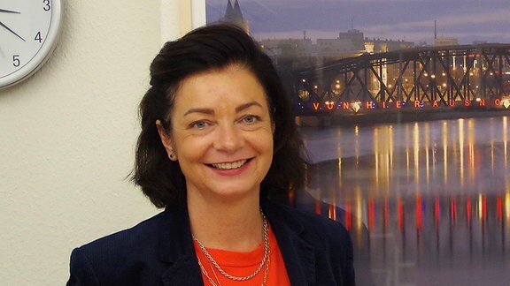 Die Kulturbeigeordnete von Magdeburg, Regina-Dolores Stieler-Hinz steht vor einem Bild, auf dem die Magdeburger Hubbrücke zu sehen ist.