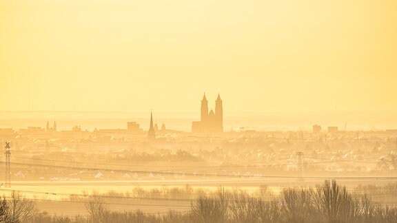 Aus der Ferne ist Magdeburg und der Magdeburger Dom im Sonnenaufgang zu sehen.