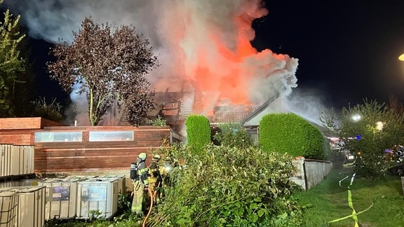 Zwei Feuerwehrleute löschen im Scheinwerferlicht einen Brand.