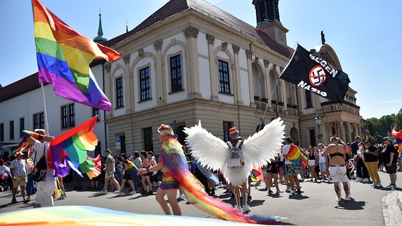Ein Teilnehmer des Christopher-Street-Day mit riesigen Engelsflügeln steht vor dem Magdeburger Rathaus und schwenkt eine Fahne mit der Schrift «Gegen Nazis». 