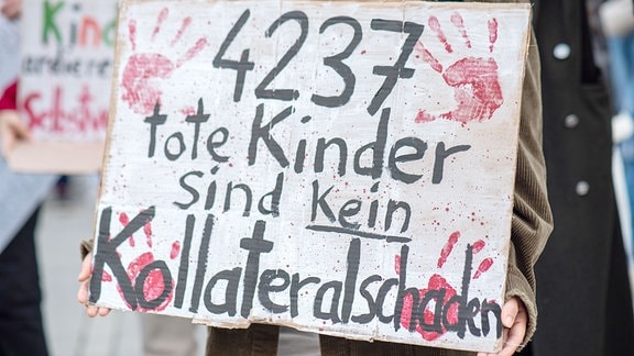 Teilnehmer auf einer Pro-Palästina-Demonstration in Magdeburg halten Schilder hoch auf denen "4237 Kinder sind kein Kollateralschaden" steht.