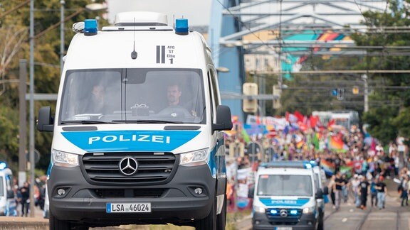Mehrere Mercedes-Transporter der Polizei fahren vor einer Demonstration 