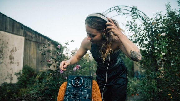 Eine Frau steht in einem Garten an einem DJ Pult