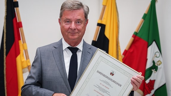 Lutz Trümper steht im Rathaus mit einer Urkunde zur Anerkennung der Ehrenbürgerwürde der Stadt Magdeburg.