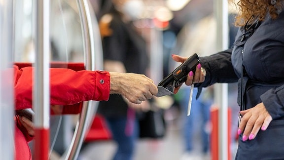 Eine Fahrkartenkontrolleurin kontrolliert mit einem elektronischen Lesegerät in der U-Bahn den Fahrschein eines Fahrgastes.
