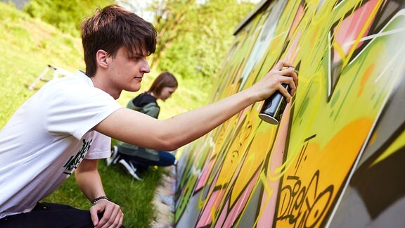 Ein Junger Mann sprüht ein Graffito an eine Fläche.