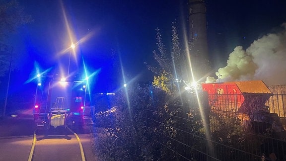 Rauchwolken ziehen von einem Firmengelände über Magdeburg, daneben sind Einsatzfahrzeuge der Feuerwehr zu sehen.