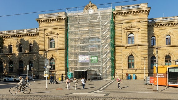 Blick auf den Hauptbahnhof in Magdeburg, ein Teil des Gebäudes ist wegen Sanierungsarbeiten verhült. Davor stehen Menschen.