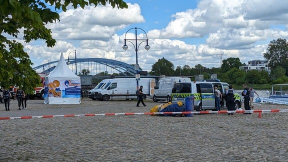 Einsatzkräfte von Polizei und DLRG mit Fahrzeugen und Boot am Elbufer, während Polizistinnen und Polizisten eine Hüpfburg zusammenbauen. 