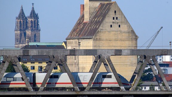 Ein ICE überquert vor den Häusern der Landeshauptstadt Magdeburg eine Elbebrücke in Richtung Hauptbahnhof.