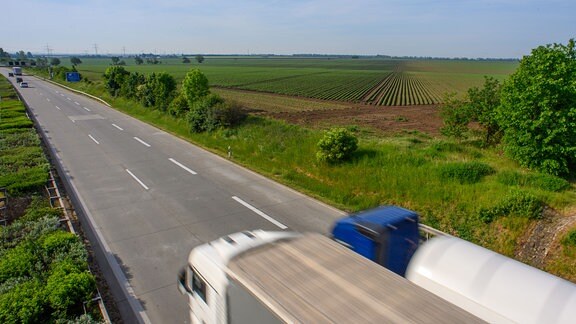 Zwei Lkw fahren auf einer Autobahn entlang einem bewirtschafteten grünen Feld
