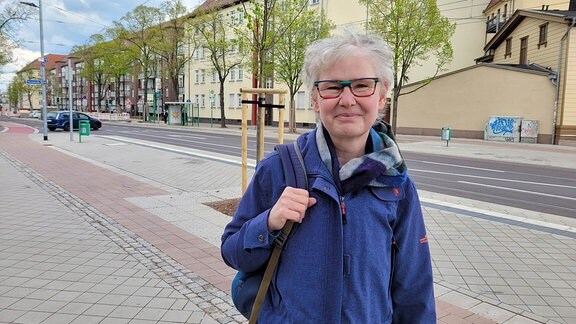 Eine Frau mit einer blauen Jacke und einer bunten Brille steht an einer Kreuzung