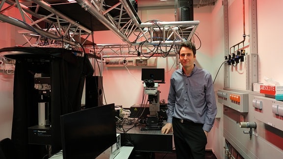 Ein Mann steht in einem Raum mit Kabeln und technischen Geräten und schaut in die Kamera