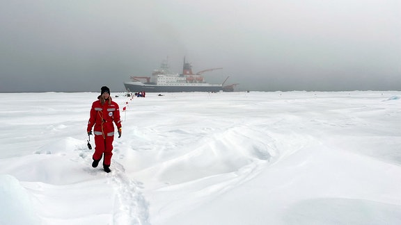 Carolin Mehlmann läuft im Nebel und Schneetreiben über den Nordpol. Im Hintergrund die Polarstern.