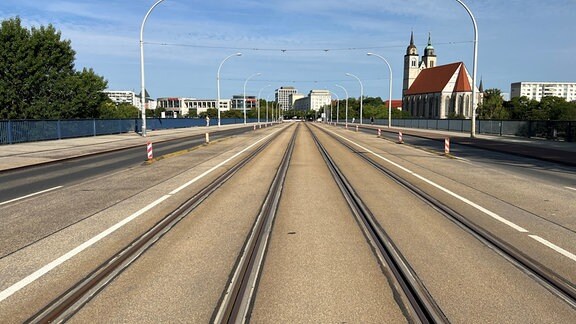 Straßenbahnschienen führen über eine Brücke in die Ferne, rechts im Hintergrund ist eine Kirche zu sehen.