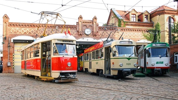 Vor den Toren eines historischen Straßenbahndepots stehen drei verschiedene Tatra-Straßenbahntriebwagen
