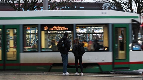 Zwei Menschen stehen vor einer Straßenbahn, die in Bewegung ist 