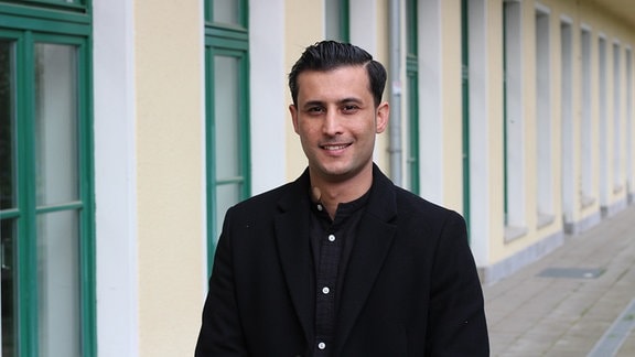 Aram Badr hat schwarze, gegelte Haare, ist schlank und trägt schwarzes Hemd und Jacke.