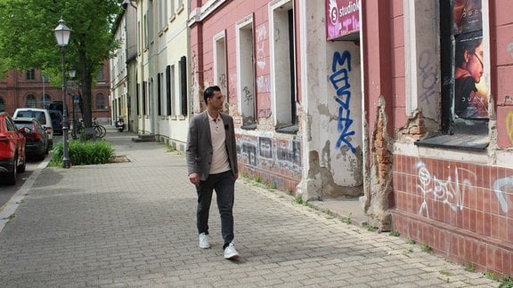 Aram Badr ist mit grauer Jeans, grauem Sakko und weißem Shirt am Moritzplatz in Magdeburg zu Fuß unterwegs