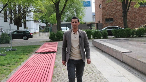 Aram Badr ist mit grauem Sakko und weißem Shirt am Moritzplatz in Magdeburg zu Fuß unterwegs.