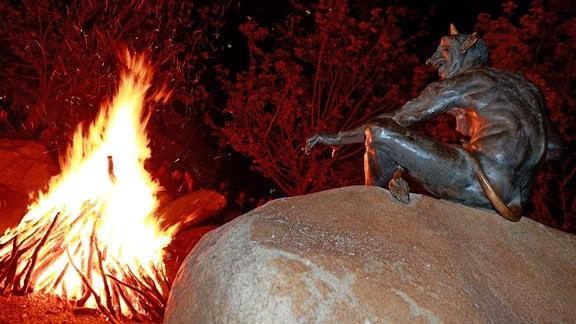 Eine Teufelsskulpur blickt auf ein Feuer. Nach vierjähriger Pause feiern Besucher Walpurgis auf dem Hexentanzplatz in Thale.