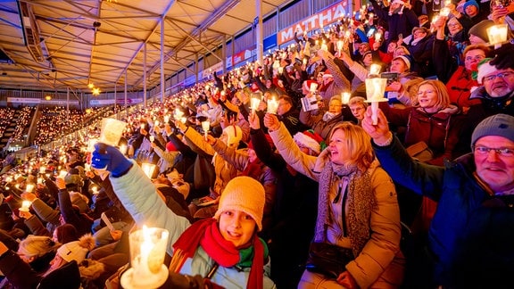 Tausende Menschen halten auf einer Stadiontribüne Kerzen hoch 
