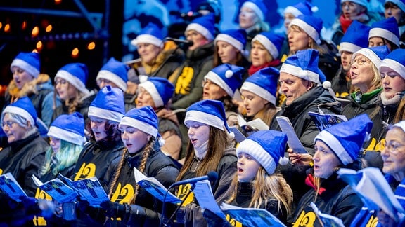 Ein Chor mit Liedblättern und blauen Weihnachtsmützen singt