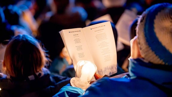 Ein Liedblatt gehalten von einer Person in blauer Kleidung mit einer Kerze