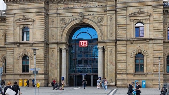 Blick auf den Haupteingang des Magdeburger Hauptbahnhofs, vor dem Reisende mit Koffern und Taschen herum laufen. 
