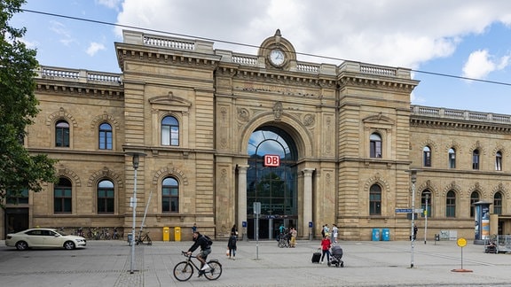 Blick auf den Haupteingang des Magdeburger Hauptbahnhofs, vor dem Reisende mit Koffern und Taschen herum laufen. 
