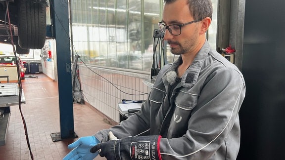 Ein Mann in einer Autowerkstatt  zieht sich Handschuhe an
