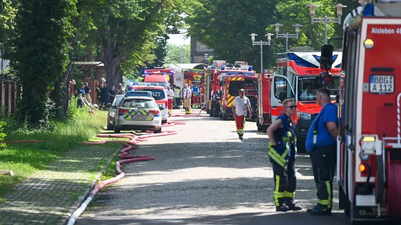 Zahlreiche Einsatzfahrzeuge der Feuerwehr stehen an einer Straße entlang aufgereiht.