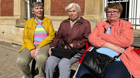 Drei ältere Frauen sitzen auf einer Bank.  