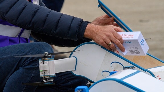 Ein Mann legt auf dem Vorfeld des Nationalen Erprobungszentrum für Unbemannte Luftfahrtsysteme des Deutschen Zentrums für Luft- und Raumfahrt (DLR) eine Pappschachtel die eine Medikamentenpackung simulieren soll in eine "Labfly"-Drohne der Firma "Diaven".