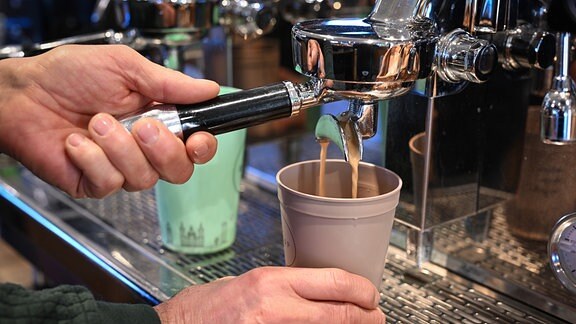 Ein Mitarbeiter eines Bio-Ladens bereitet einen Kaffee zu, der in einen Mehrwegbecher fließt.