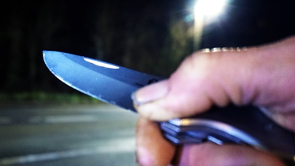 Eine Person hält bei Dunkelheit an einer Straße ein Messer in der Hand.