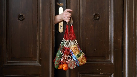 Einkaufsnetz mit Lebensmitteln wird durch einen Türspalt gehalten