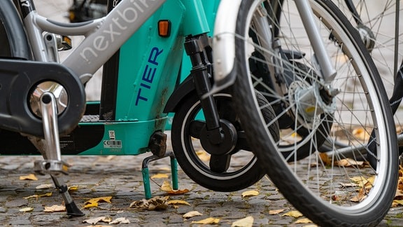 E-Tretroller des Anbieters Tier und ein Leihfahrrad von Nextbike stehen nebeneinander auf einem Gehweg. Der für seine türkisblauen E-Tretroller bekannte Anbieter Tier Mobility übernimmt den Leipziger Fahrradverleiher Nextbike.
