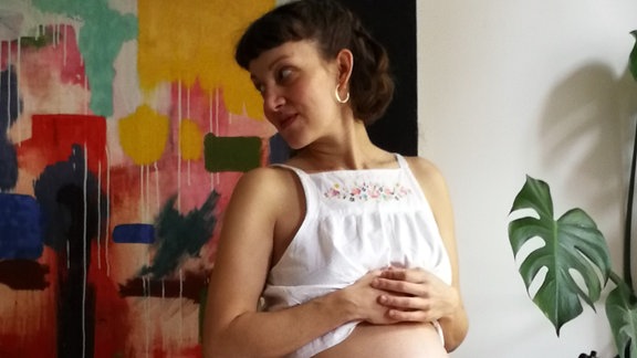 Eine junge Frau zeigt ihren Babybauch.