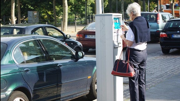 Eine ältere Frau wirft Münzen in einen Parkscheinautomat.