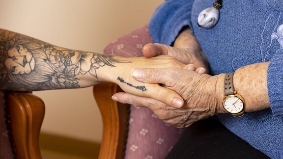 Die Hand einer Altenpflegerin hält liebevoll und wärmend die Hände einer Seniorin